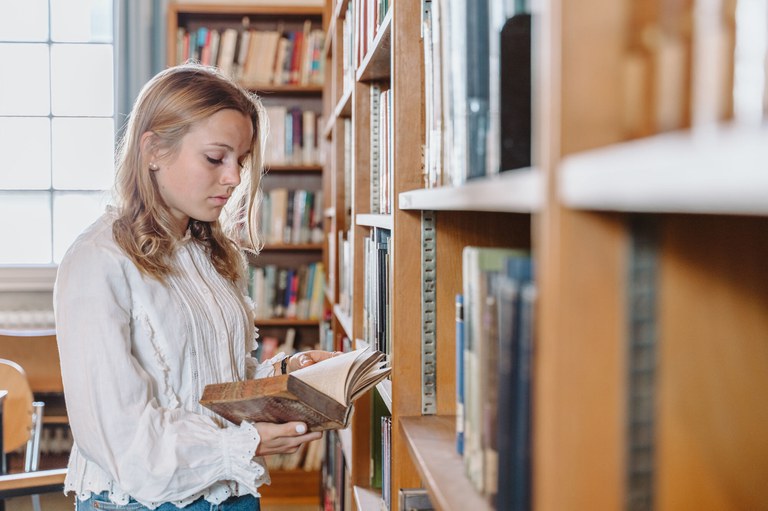 Eine Studentin sucht sich in der Bibliothek ein Buch heraus.